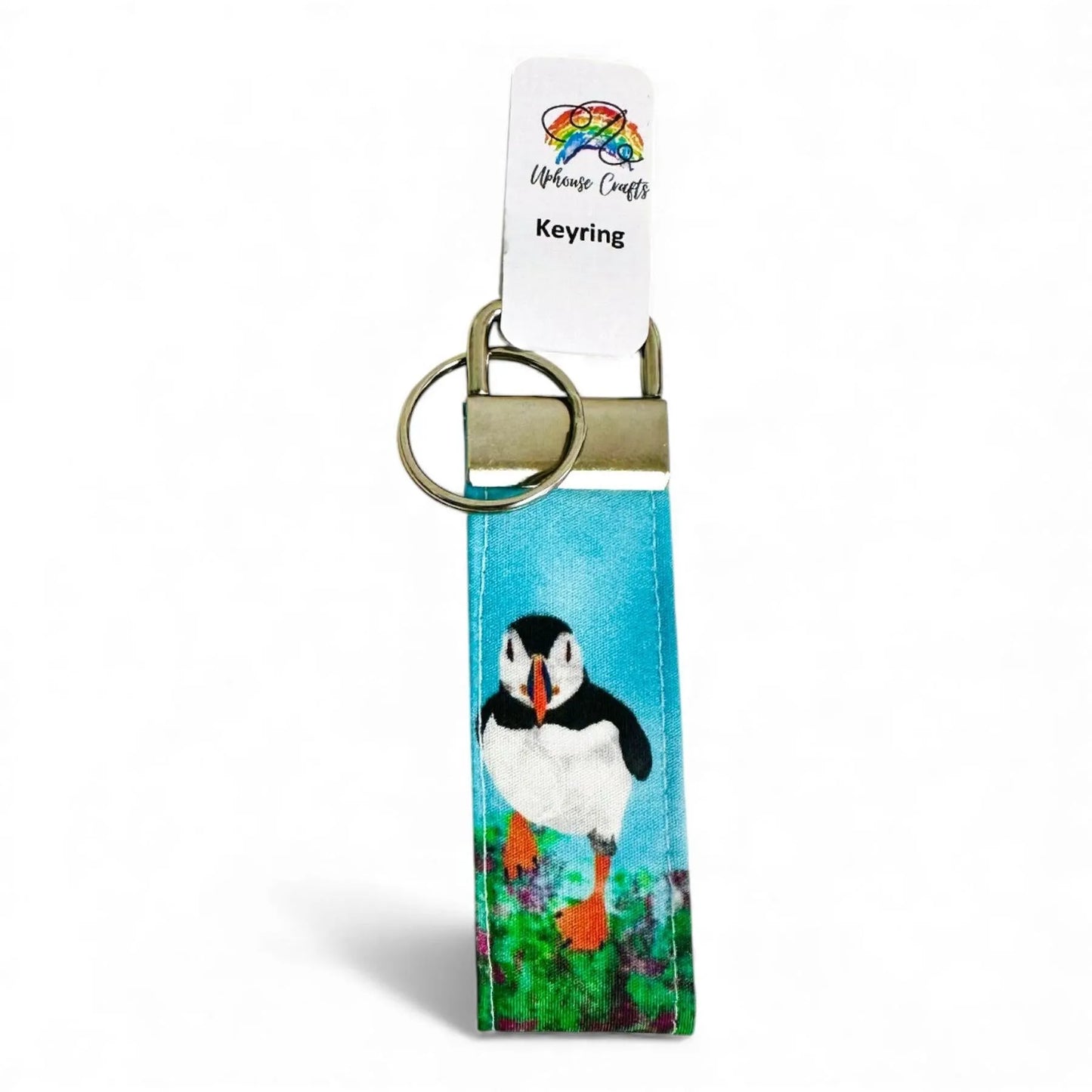 Fabric keyring featuring a colorful puffin illustration on a blue background with a metal clasp.