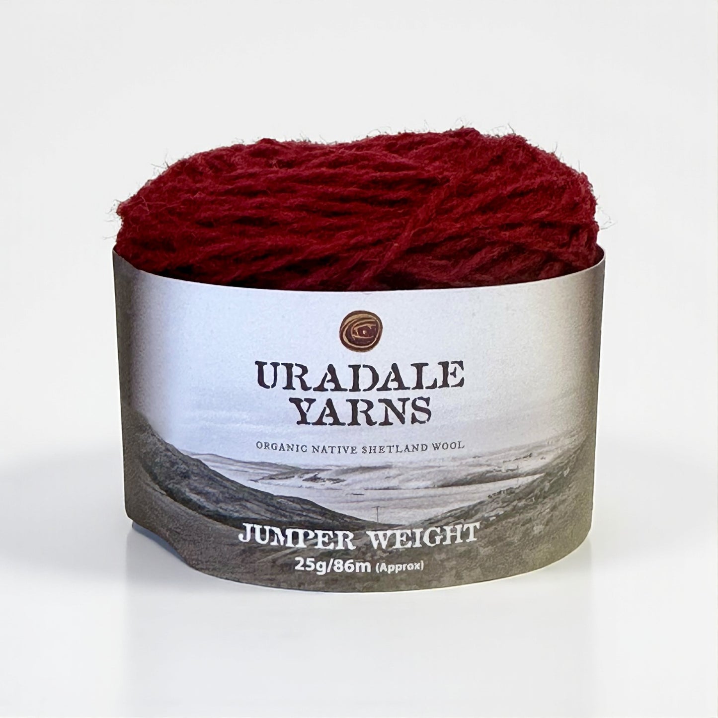 A ball of deep red Uradale Shetland wool yarn with a landscape-themed paper label.