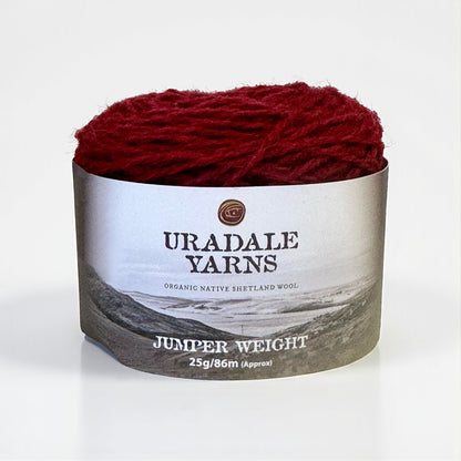 A ball of deep red Uradale Shetland wool yarn with a landscape-themed paper label.