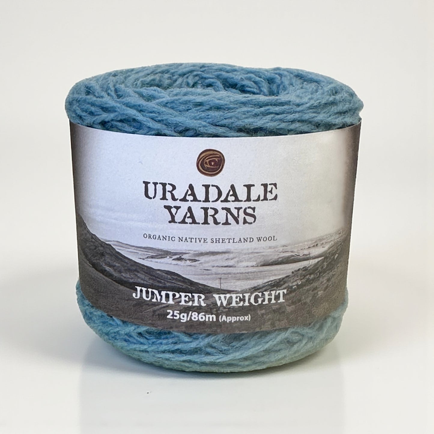 A ball of blue Uradale Speedwell Shetland wool yarn with a landscape-themed paper label.