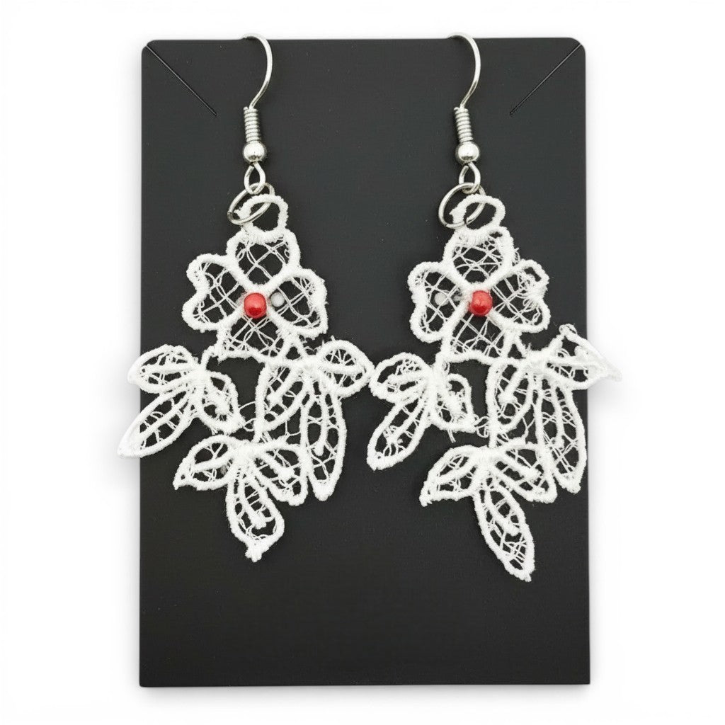 White embroidered flower lace earrings with red bead centers and silver-plated hooks on a black card.
