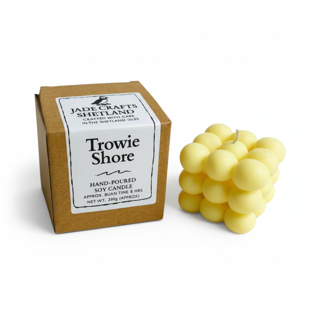 A yellow bubble-shaped soy candle sits next to its brown cardboard box with a white label.